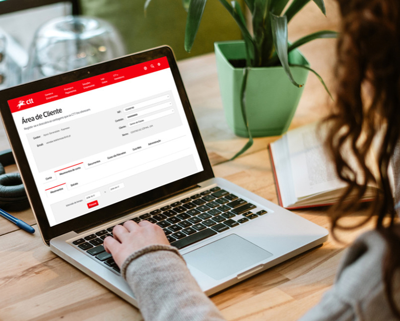 Pessoa a usar um portátil, numa mesa com uma chávena de café, auscultadores e uma planta.