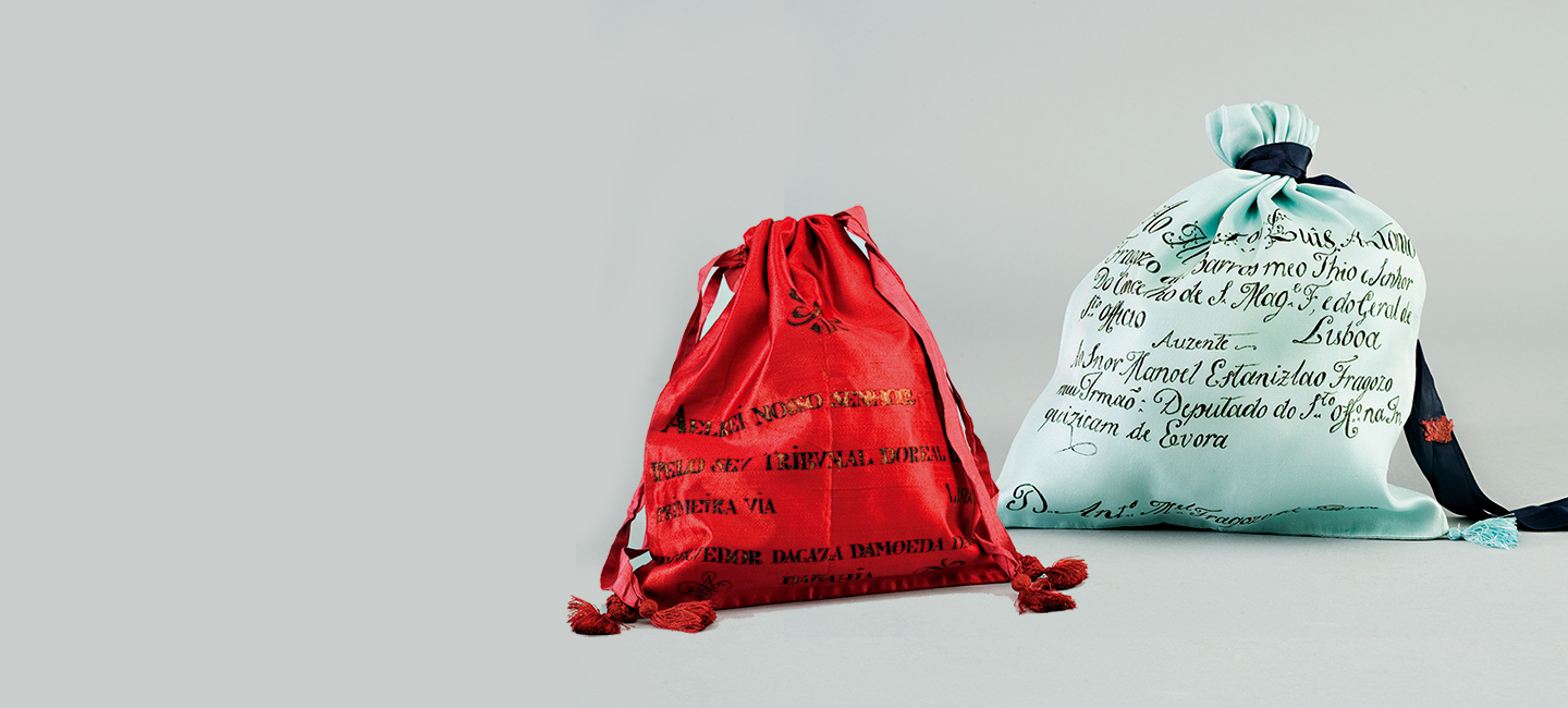 Duas mochilas de cordão, uma vermelha e outra branca com texto preto, sobre fundo cinza.