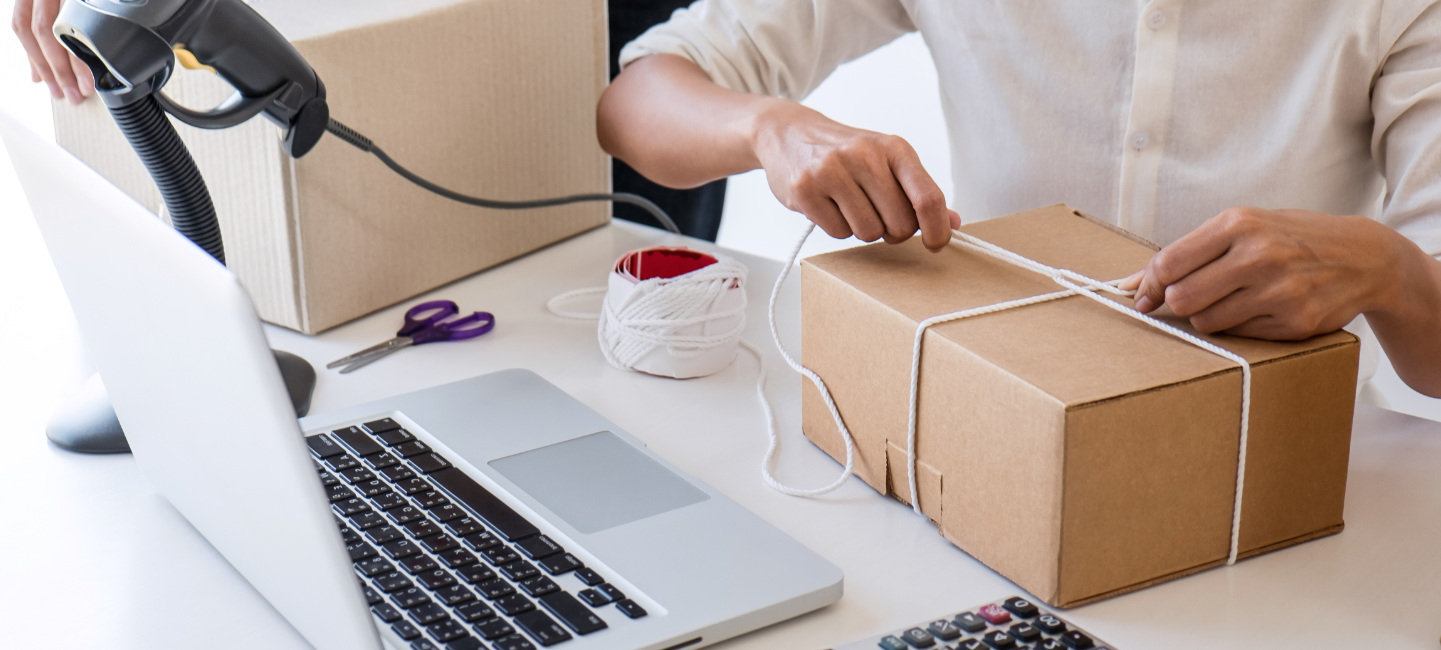 Duas pessoas embalam caixas com computador, scanner, tesoura e outros itens em cima da mesa.