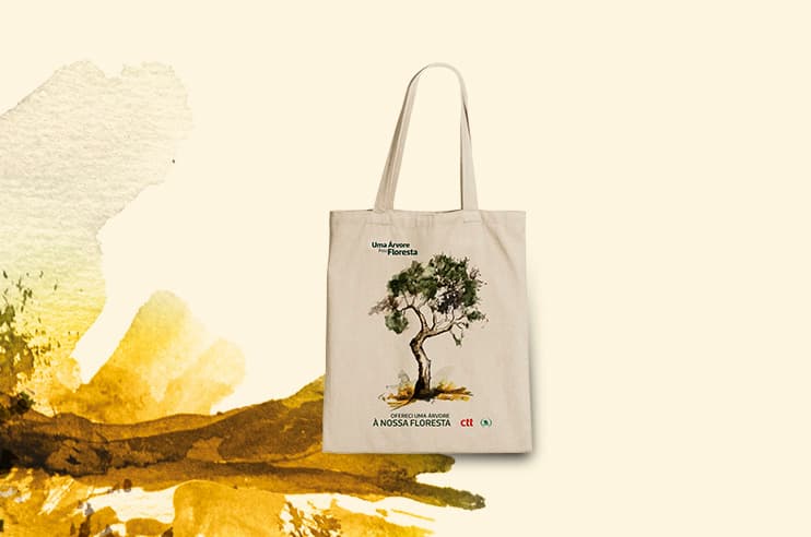Saco de tecido bege com alças. ilustração de uma árvore ( Oliveira)  com o texto “Ofereci umá árvore à nossa floresta”. O fundo é claro, em bege ao branco e manchas artísticas em tons de castanho  e verde.
